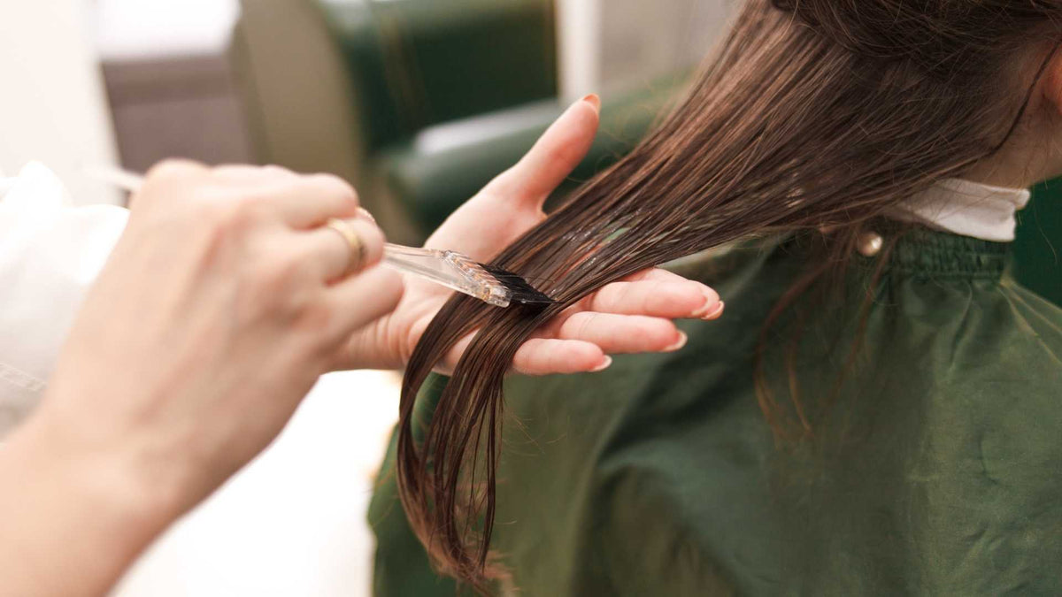 Hairdresser applying conditioner to the lengths and ends of wet brown hair