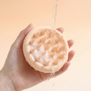 Hand holding a textured soap bar with water being poured over it against a beige background