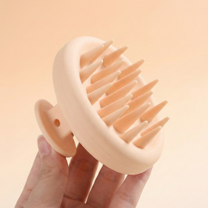 Hand holding a beige scalp massager against a beige background