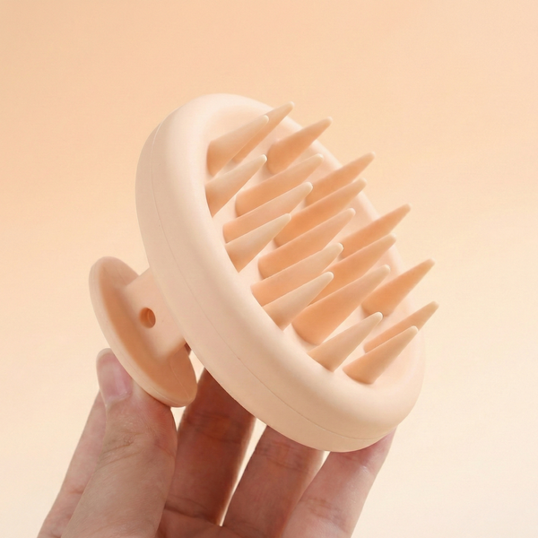 Hand holding a beige scalp massager against a beige background