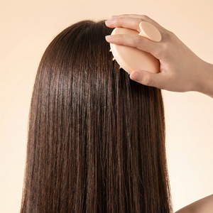 Person brushing long brown hair with a round brush on a beige background