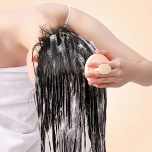 Person with wet, soaped hair holding a bar of soap against a beige background